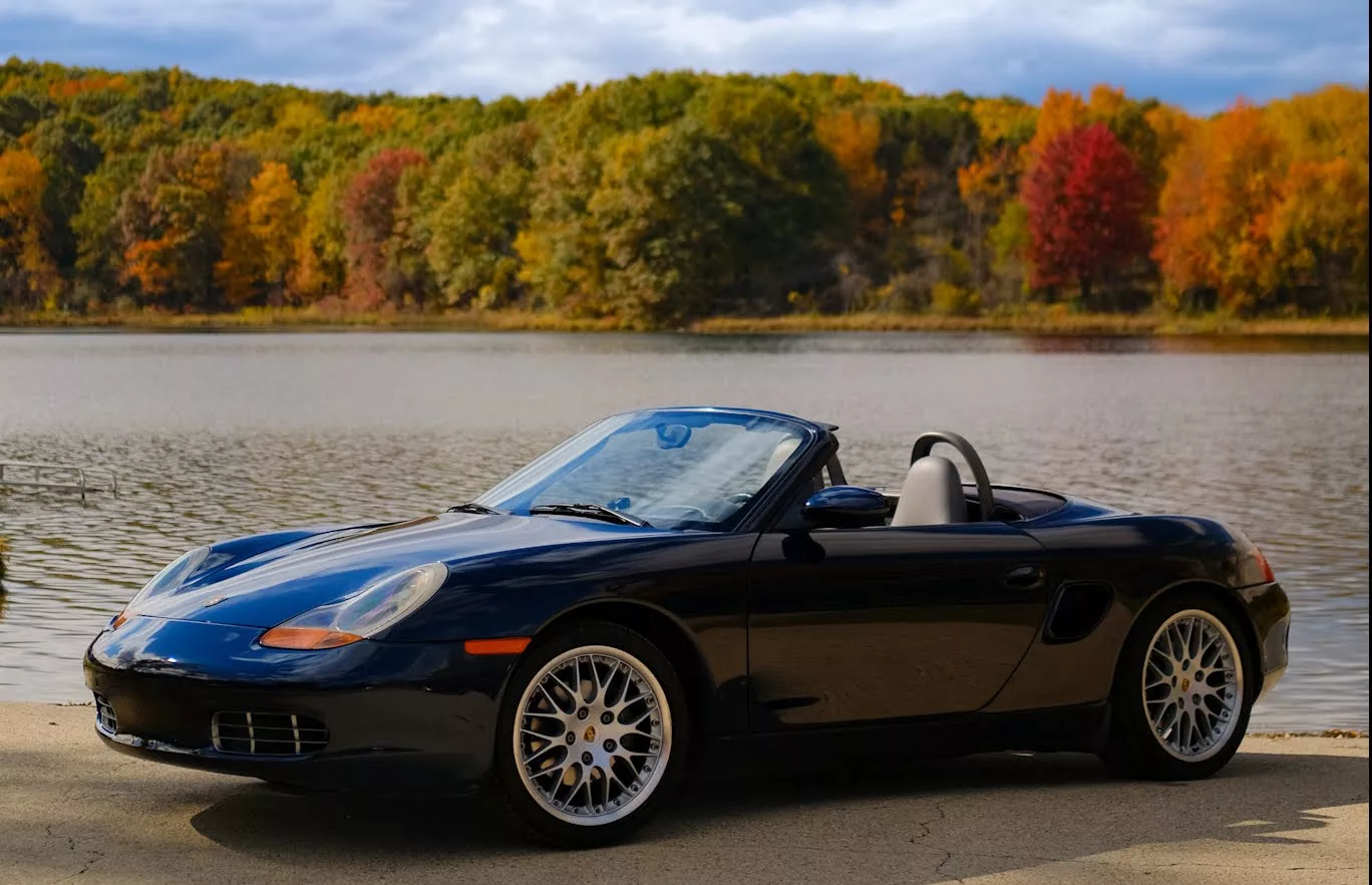 Dark blue Porsche Boxster by a lake in autumn
